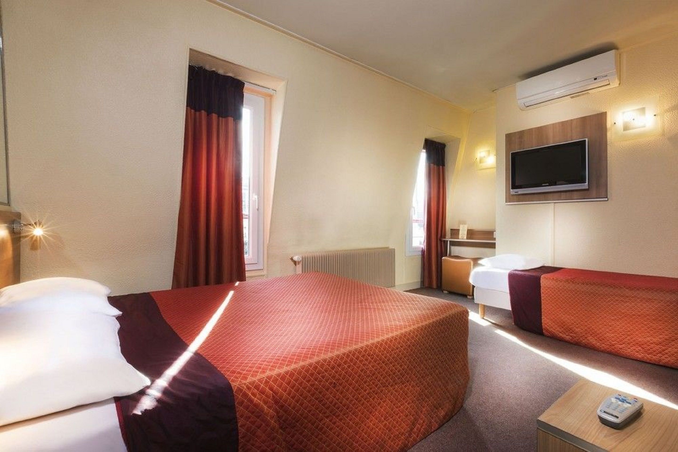 A hotel room with two beds, a TV, a heater, and a window with curtains.
