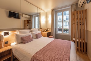 A hotel room with a large bed, bedside tables, a TV mounted on the wall, and a window with a view of buildings. - Hotel de France Quartier Latin (Paris)