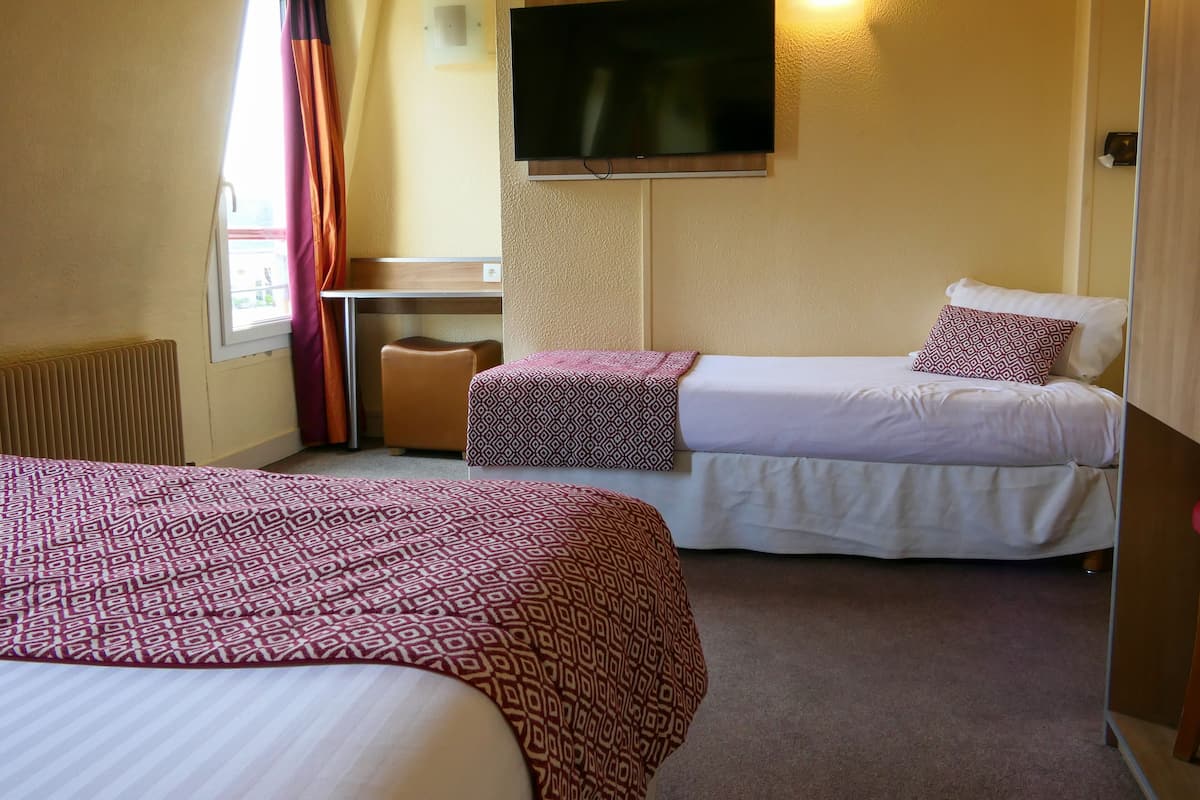 Een hotelkamer met twee bedden, een bureau, een televisie en een raam met gordijnen.