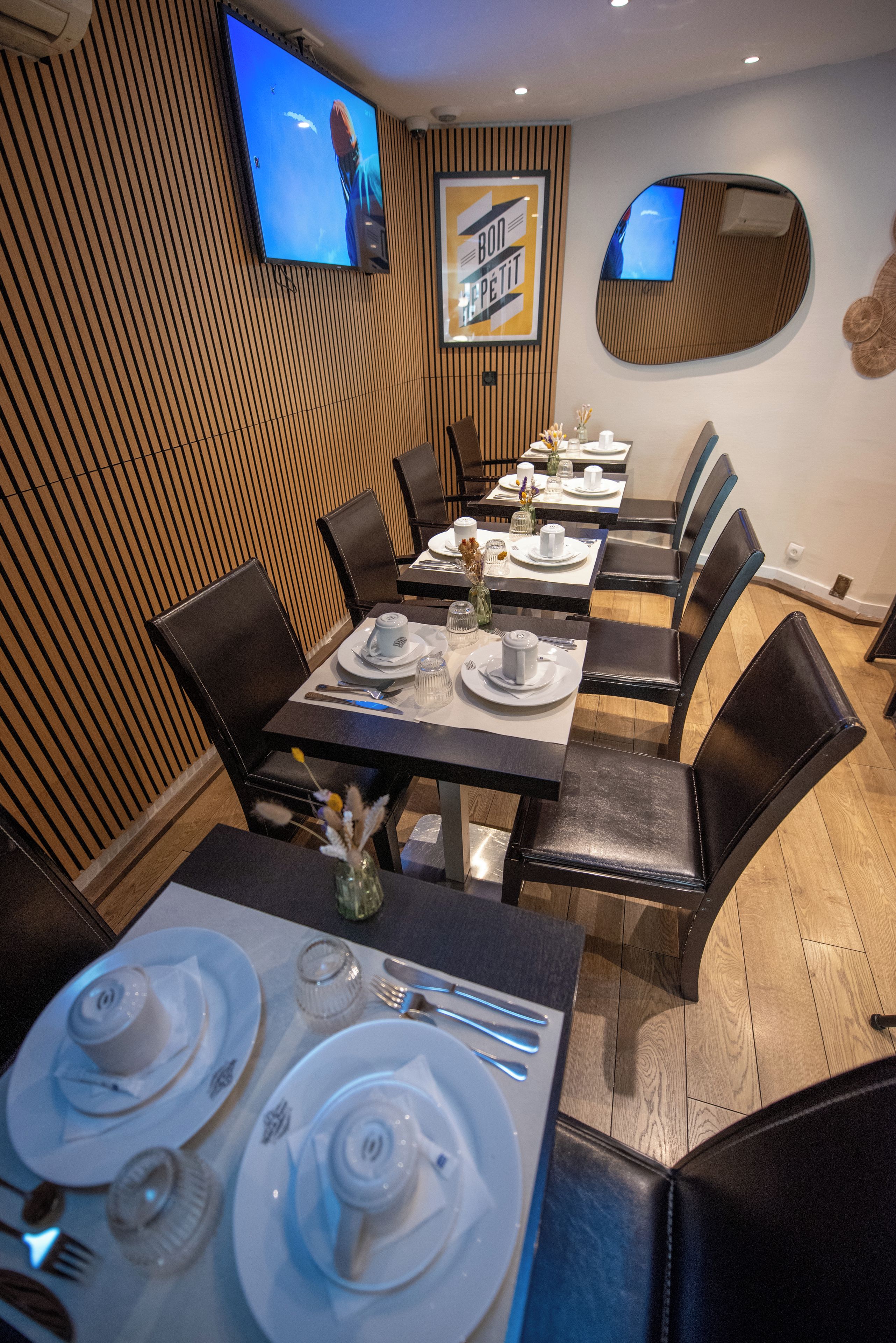 Un restaurante con una decoración moderna, que cuenta con paneles de madera en las paredes, mesas redondas con vajilla blanca y sillas de cuero negro.