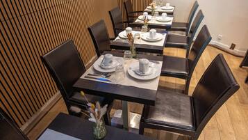 Un restaurante con una decoración moderna, que cuenta con paneles de madera en las paredes, mesas redondas con vajilla blanca y sillas de cuero negro.