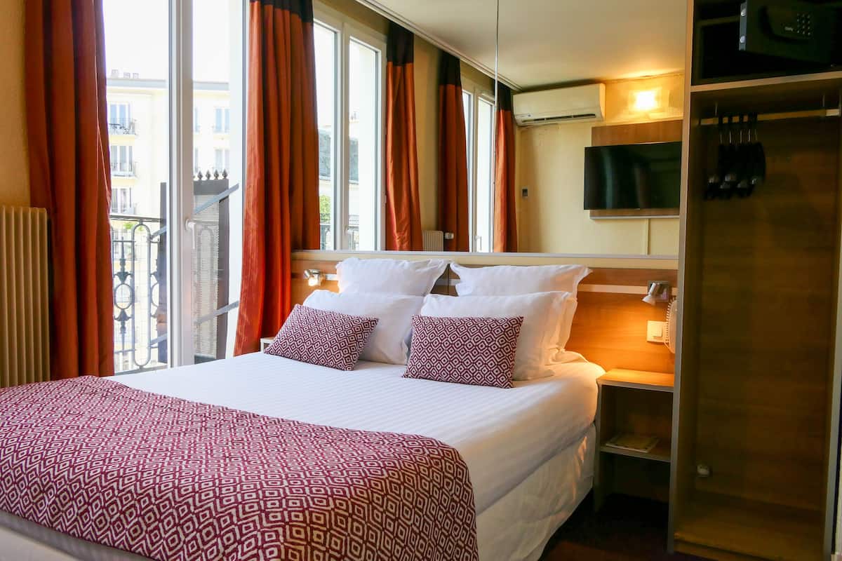 Een hotelkamer met een groot bed, een nachtkastje met lamp, een kast en uitzicht op het balkon.