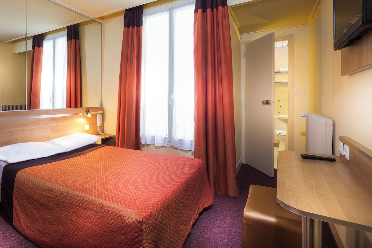 Een hotelkamer met een bed, nachtkastje en een bureau met stoel.
