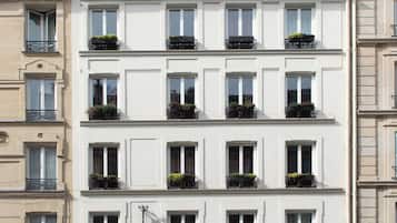 Un hotel de varios pisos con un estilo arquitectónico europeo clásico, que presenta balcones con barandas metálicas y plantas en macetas.