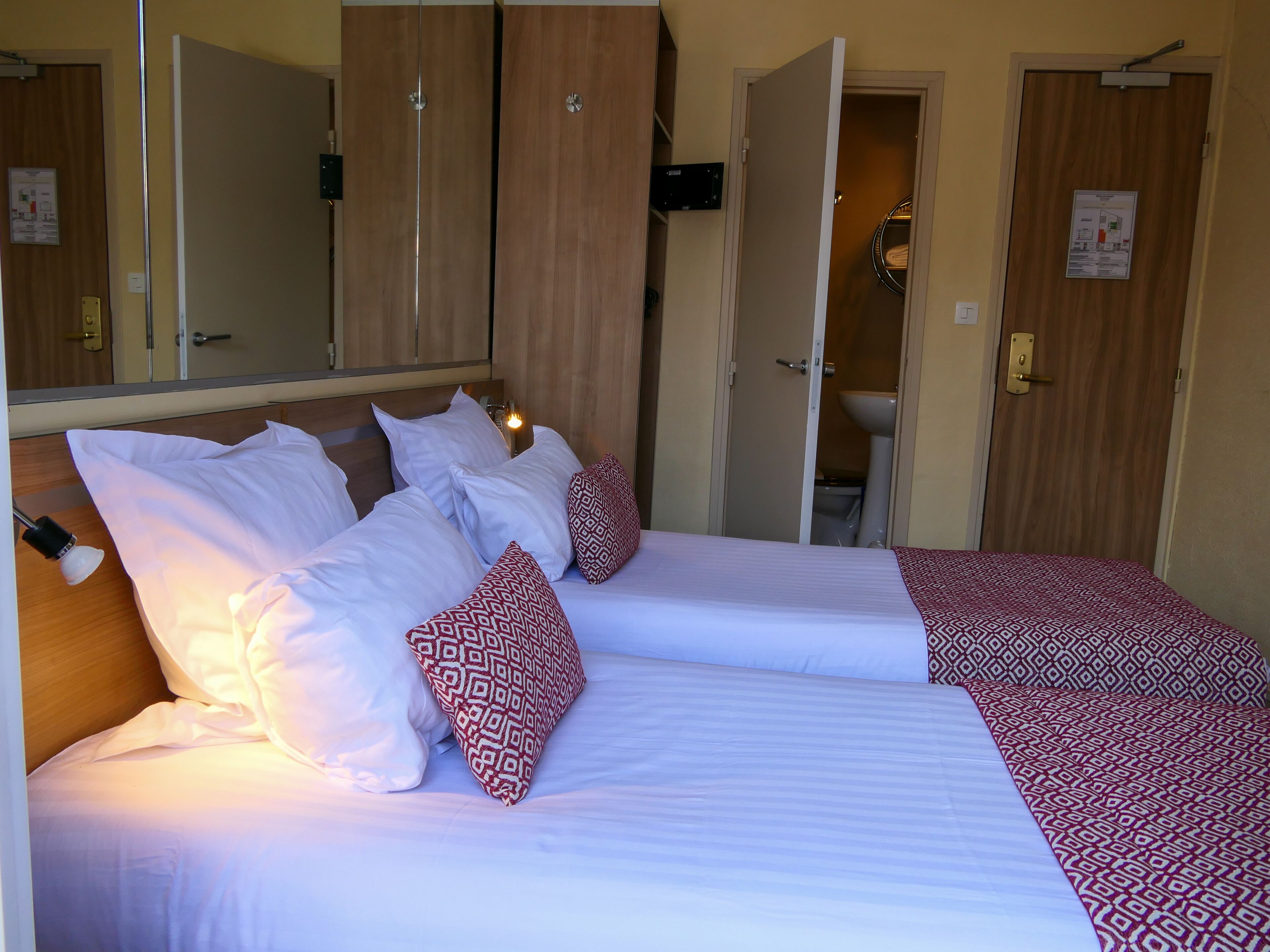 A double bed with white and patterned pillows, a wooden headboard, and a mirror above.