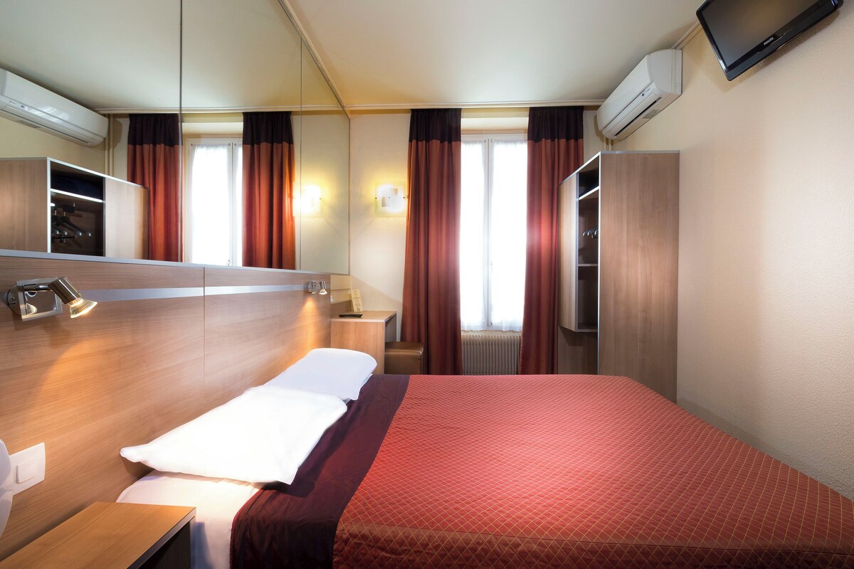 Een hotelkamer met een groot bed, nachtkastje, spiegel, televisie en airconditioning.