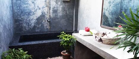 A bathroom with a large bathtub, a small sink, and a mirror. There are plants and a flower on the counter.