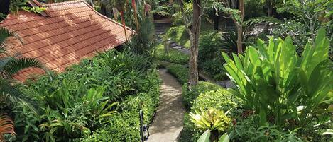 A lush garden with a pathway leading to a building with a red-tiled roof.