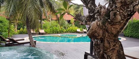 A pool area with lounge chairs, a circular hot tub, and lush greenery.