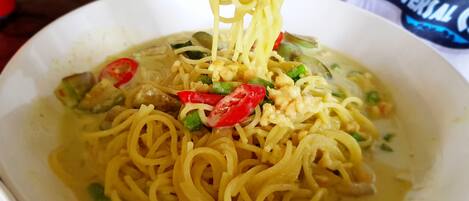 A bowl of noodles with vegetables and meat, being lifted with a fork.