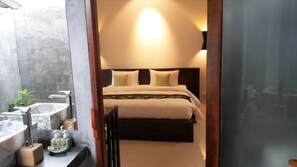 A bedroom with a bed, bedside table, and a bathroom with a sink and mirror.