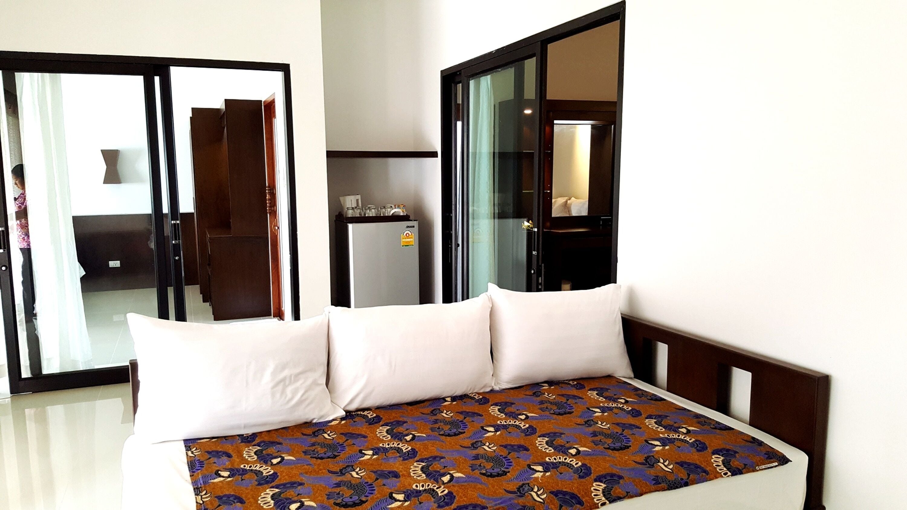 Una habitación de hotel con cama, minibar y puerta corrediza de vidrio que da a un balcón.