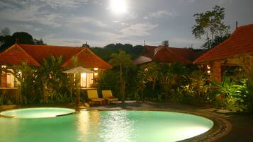 A pool area with a circular pool, lounge chairs, and buildings with red-tiled roofs.