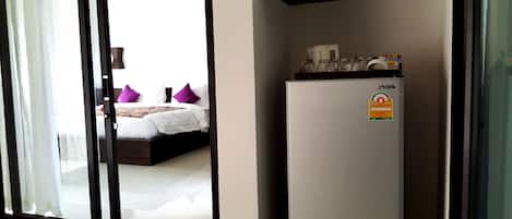 Una habitación de hotel con cama, refrigerador y puerta corrediza de vidrio que da a un balcón.