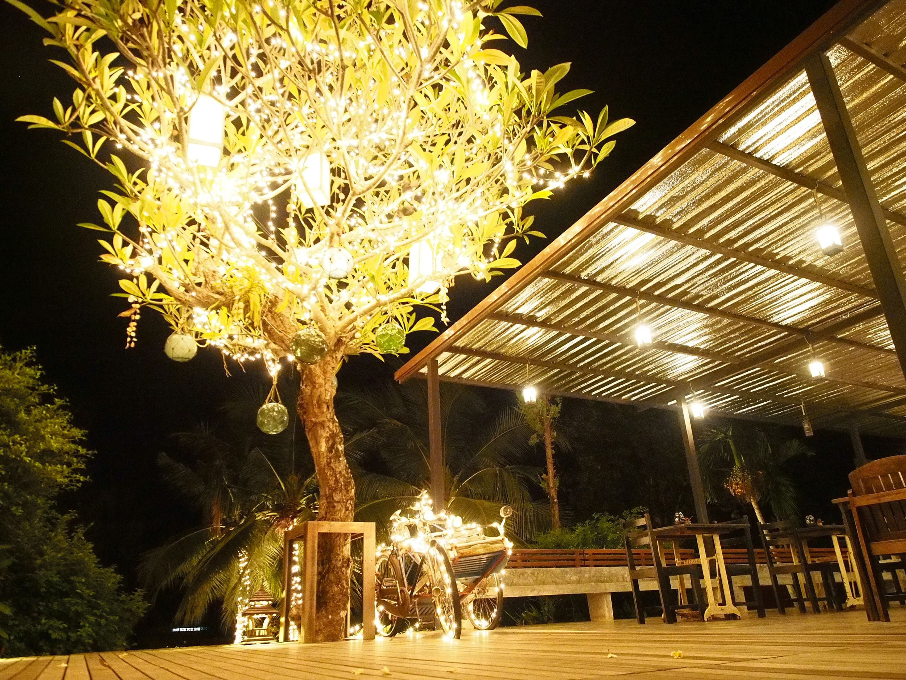 A tree decorated with lights and ornaments, a covered outdoor seating area with tables and chairs, and a wooden deck.
