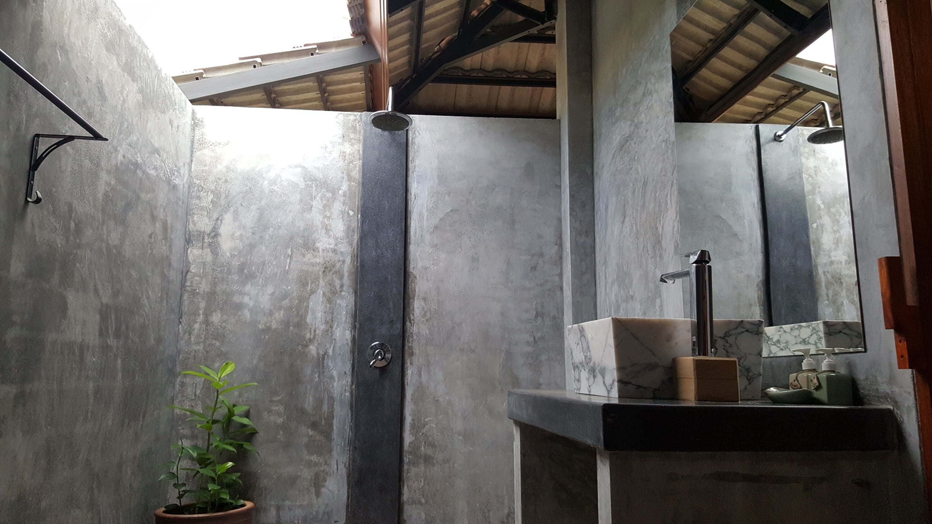 A bathroom with a concrete wall, a shower, a sink with a marble countertop, and a potted plant.