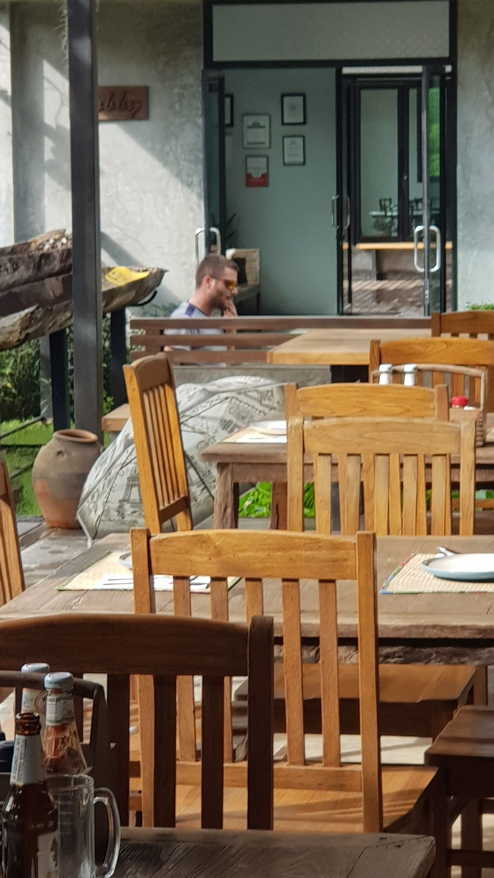 An outdoor seating area with wooden tables and chairs, a large vase, and a bottle on the table.