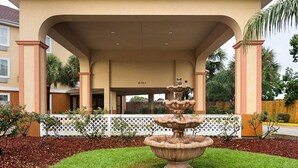 Un bâtiment doté d’un porche, d’une fontaine décorative et d  ’une clôture blanche en bois.