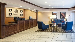 Un espace d’accueil d’hôtel avec un comptoir de réception en bois, des sièges bleus et des tableaux encadrés accrochés aux murs.