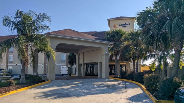L’entrée d’un hôtel Comfort Inn, avec une allée couverte, des palmiers et un ciel bleu dégagé.