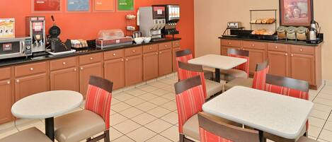 A breakfast area with a coffee machine, toaster, and a display of pastries.