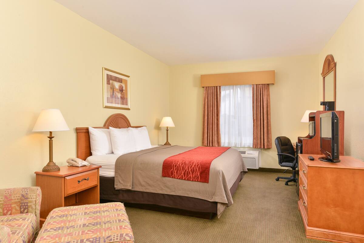 Une chambre d’hôtel comprenant un lit, deux tables de chevet avec des lampes, un bureau avec un ordinateur et une chaise.