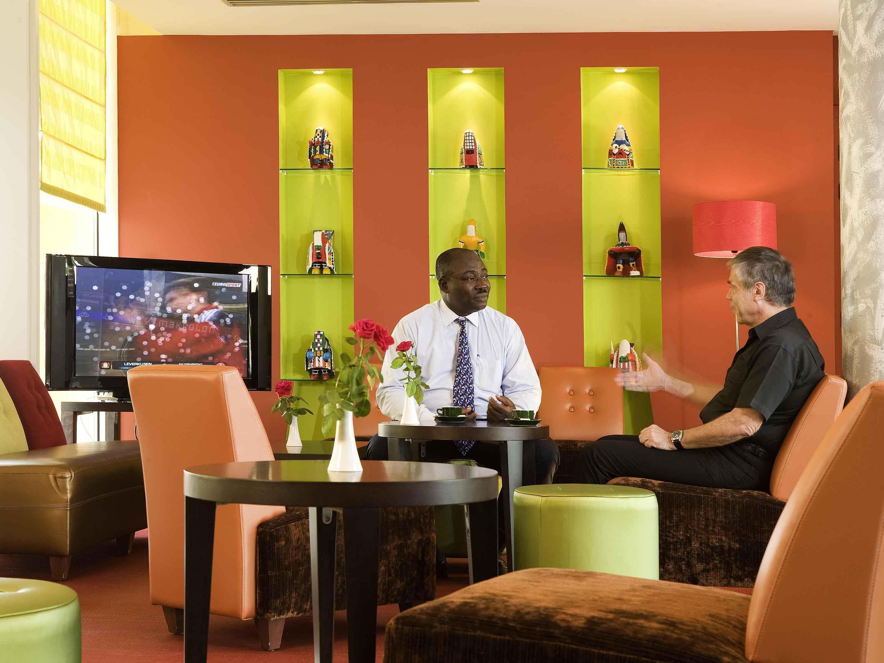 A hotel lobby with a television, seating area, and decorative items on shelves.