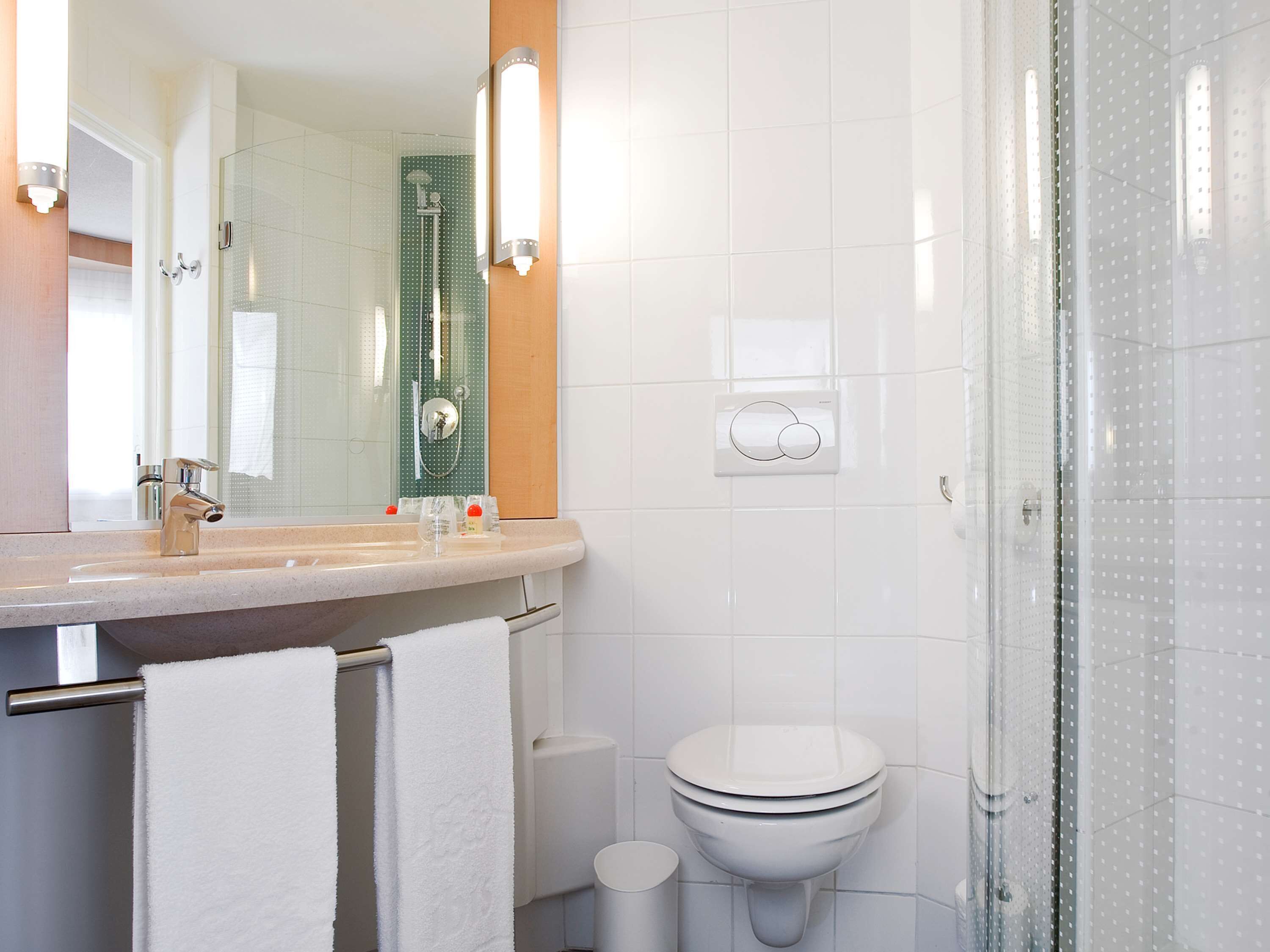 Un baño moderno con cabina de ducha de vidrio, lavamanos blanco con espejo y un inodoro.