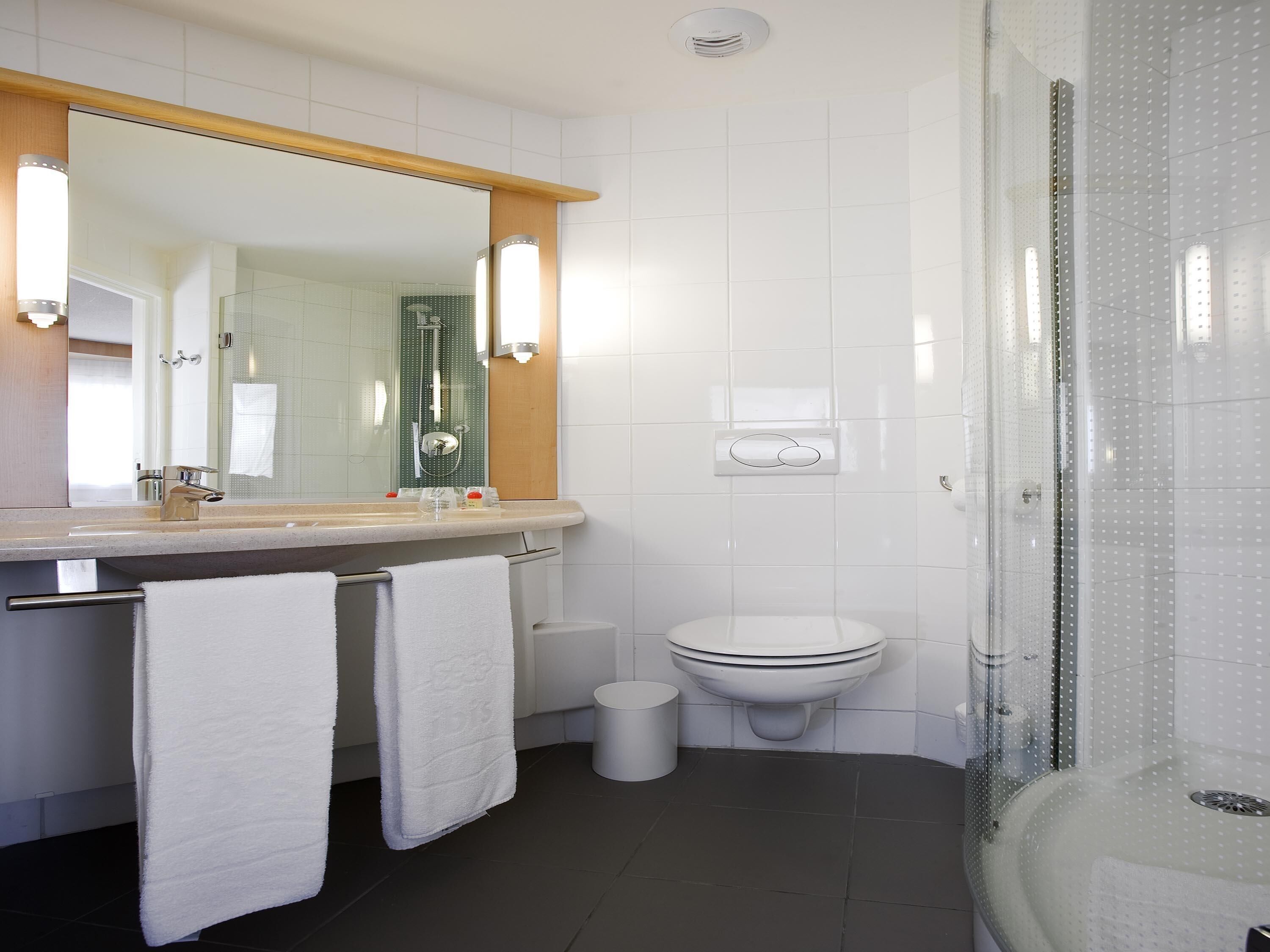 A modern bathroom with a large mirror, a toilet, a shower enclosure, and a towel rack.