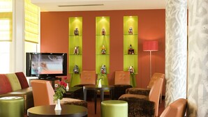 A modern lounge with green and brown upholstered seating, a flat-screen TV, and red pendant lighting. - ibis Cotonou (Cotonou)