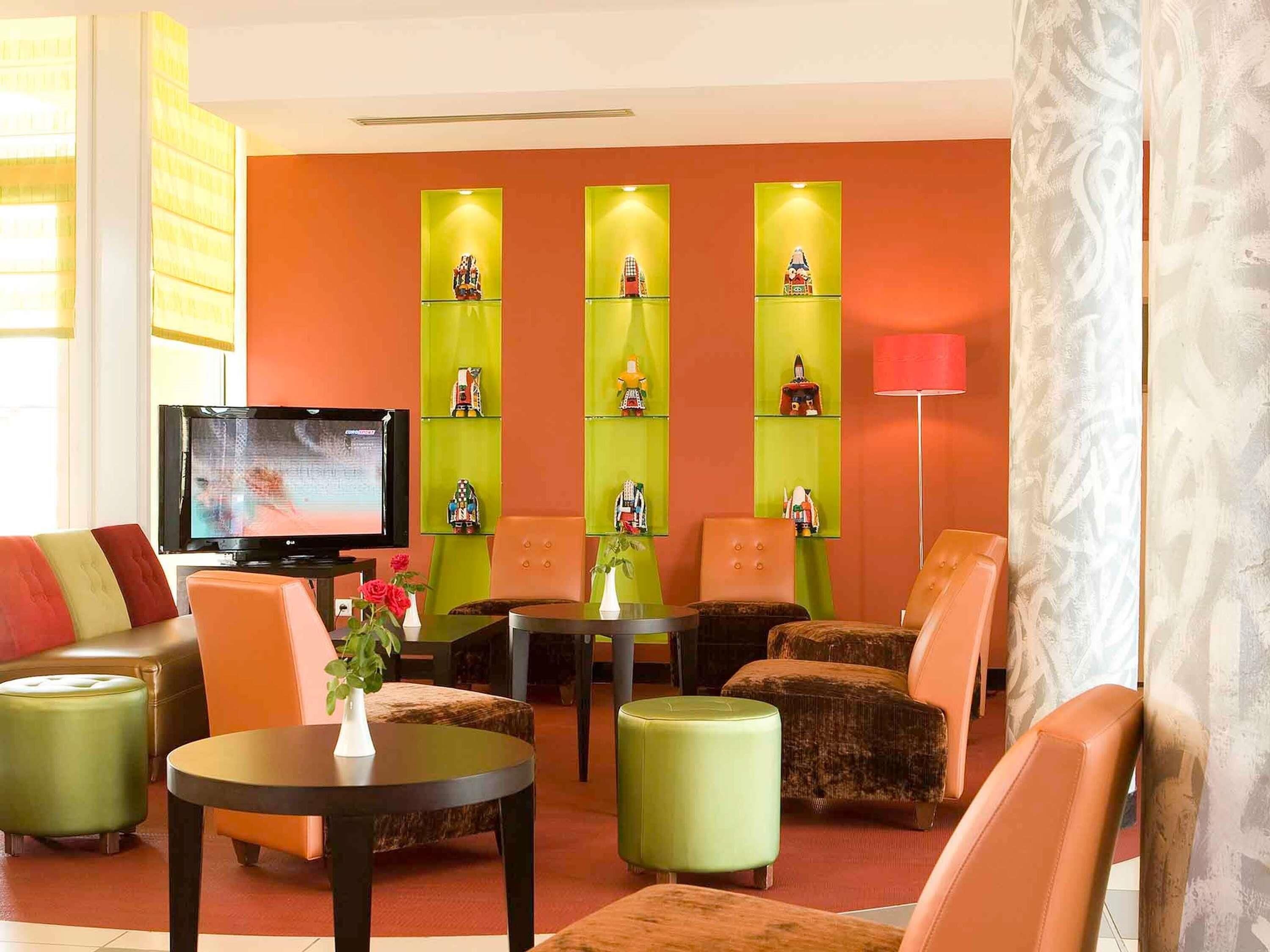 A hotel lobby with a television, green and orange seating, and decorative shelves.