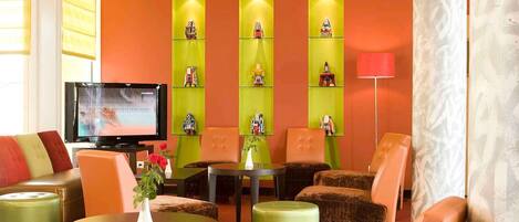 A hotel lobby with a television, green and orange seating, and decorative shelves.