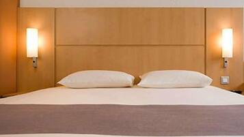 Una habitación de hotel con cabecera de madera, dos lámparas de noche y una cama con ropa blanca.