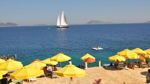 A beach with yellow umbrellas, a sailboat, and a clear blue sea.