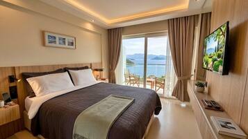 A hotel room with a large bed, a TV, a desk, and a view of the sea.