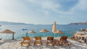 A seaside terrace with wooden lounge chairs and thatched umbrellas overlooking the sea.