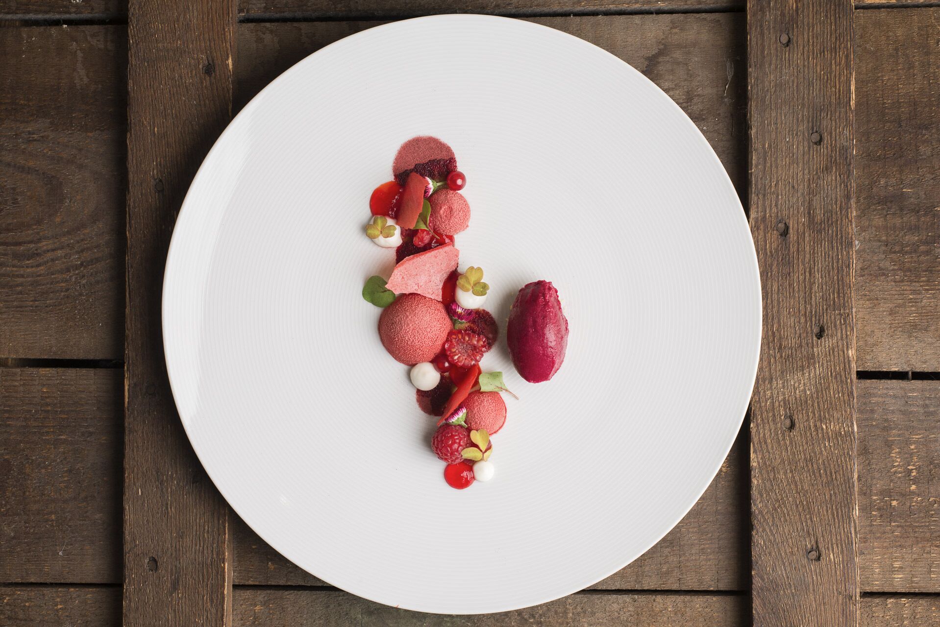 Plat blanc amb diverses fruites i petits objectes decoratius sobre una taula de fusta.