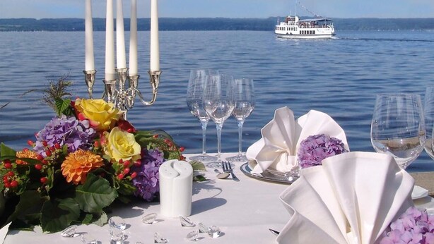 A table set for a meal with a view of a body of water and a boat in the distance. - Romantik Hotel Chalet am Kiental (Herrsching am Ammersee)