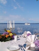 Mesa posta para refeição, vista para a água e barco ao longe.