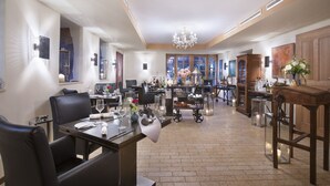 A spacious dining area with a high ceiling, a chandelier, and a view of the outdoors through large windows. - Romantik Hotel Chalet am Kiental (Herrsching am Ammersee)