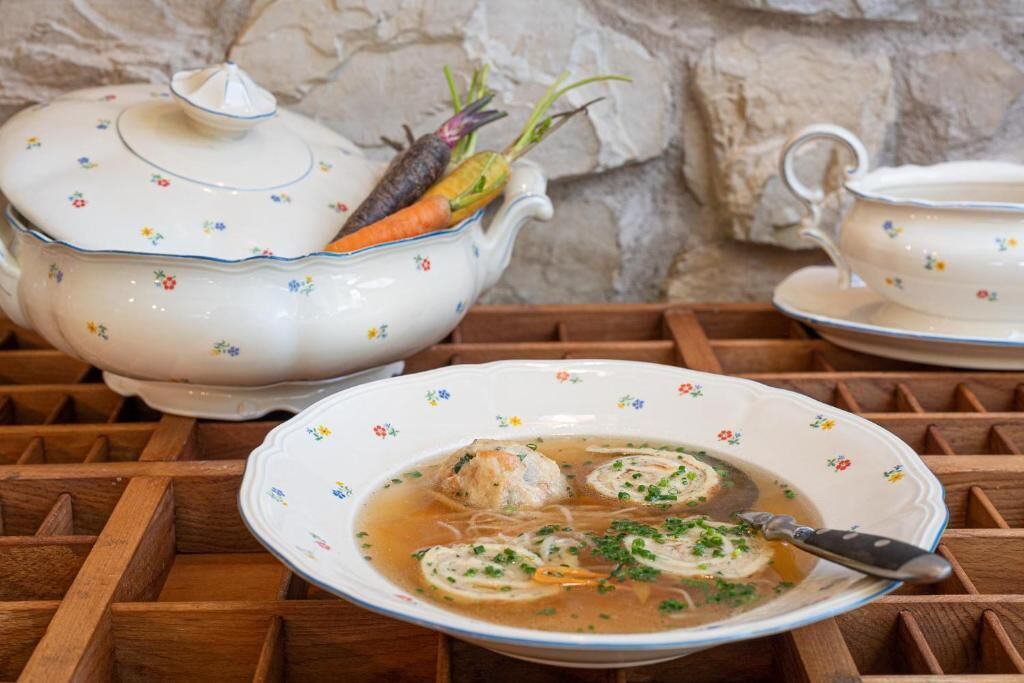 Une table avec une théière, une tasse à thé et un bougeoir à thé, ainsi qu’un bol de soupe contenant des boulettes et des herbes.