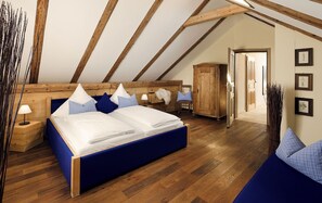 A bedroom with a wooden ceiling, a large bed with blue bedding, a wooden wardrobe, and a nightstand with a lamp. - Romantik Hotel Chalet am Kiental (Herrsching am Ammersee)
