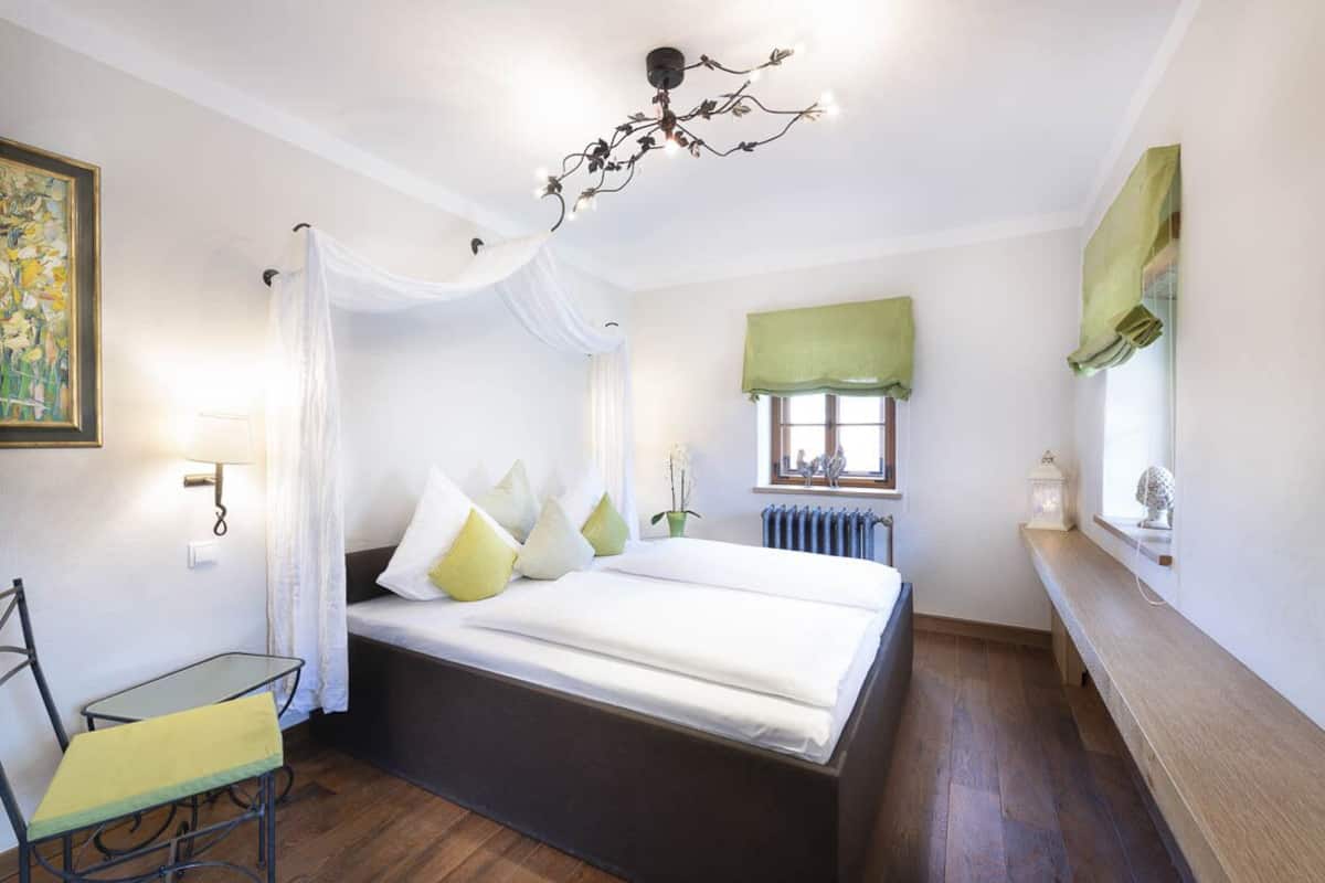 Une chambre à coucher comprenant un lit, une chaise, une table, une fenêtre avec des rideaux, un radiateur et un lustre.
