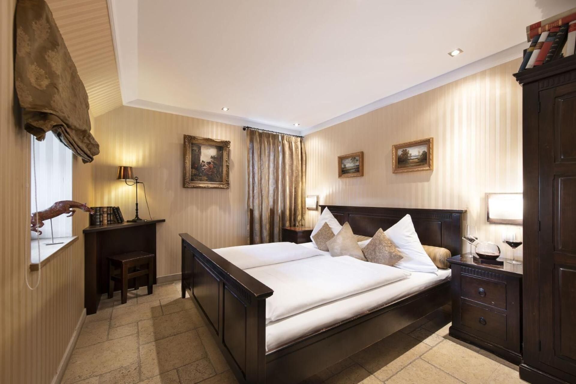A hotel room with a large bed, a wooden nightstand, a desk with a lamp, and a wardrobe.