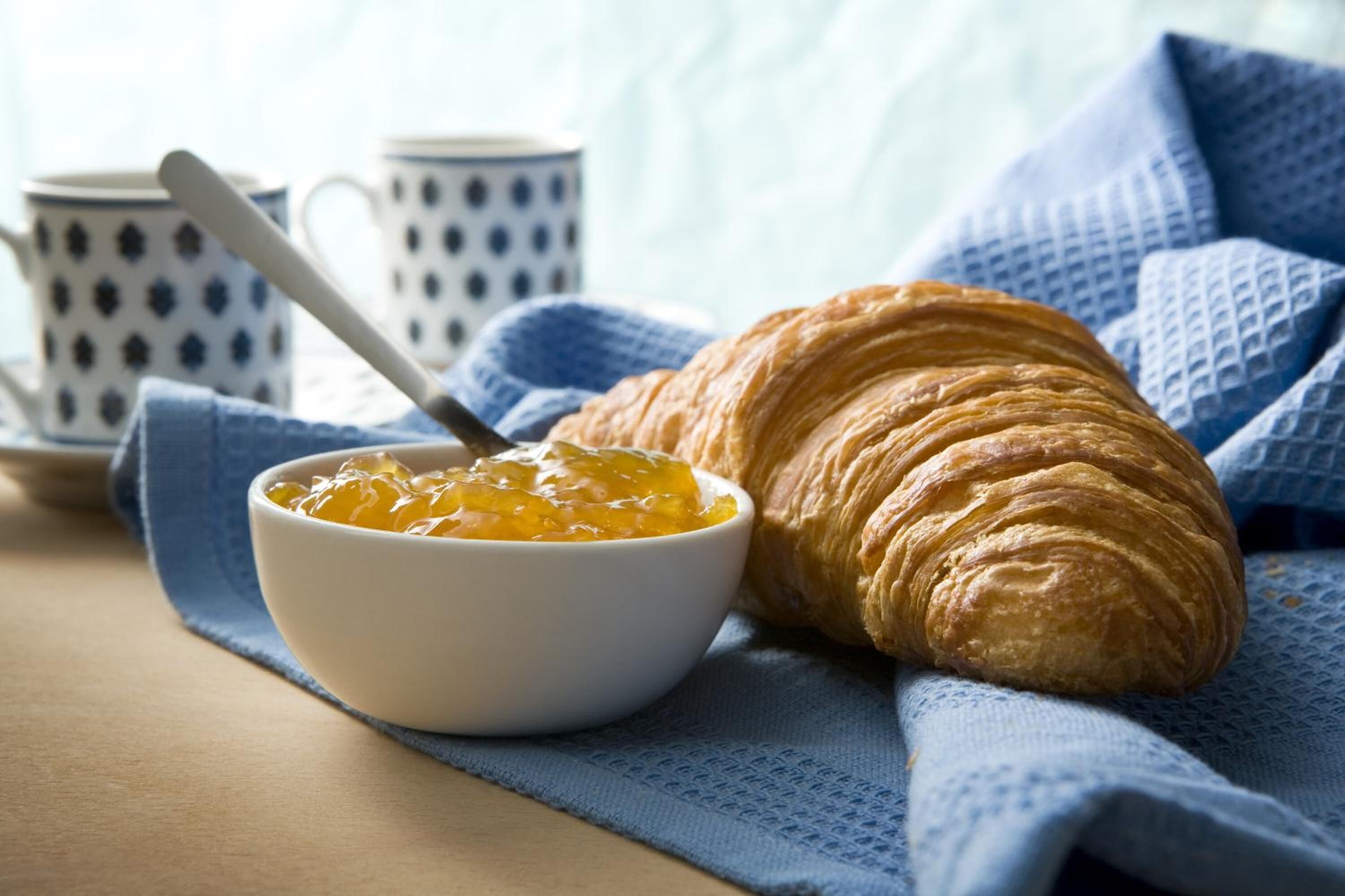 Ein Croissant und eine Schale Marmelade auf einem blauen Tuch.