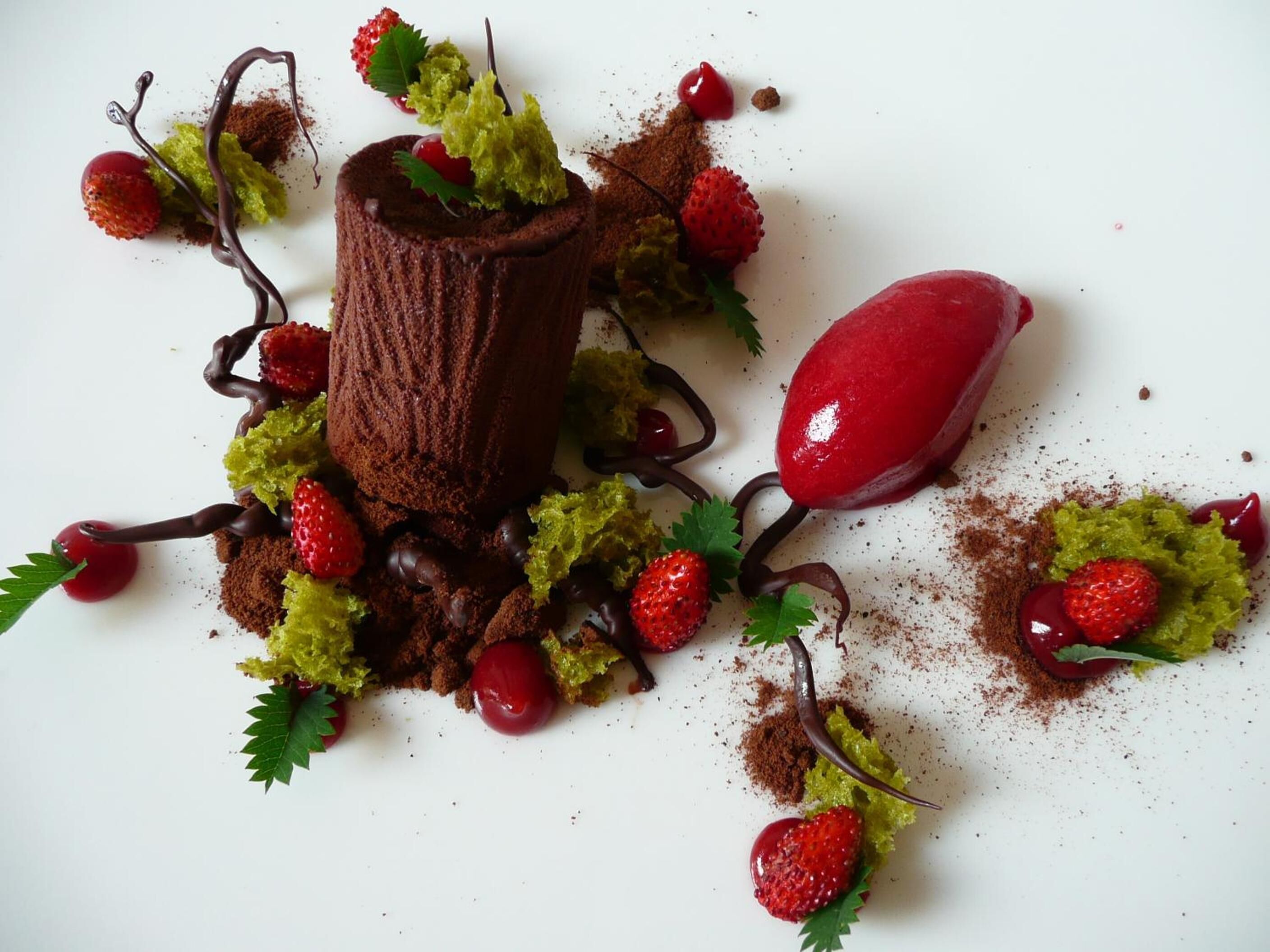 Un postre con mousse de chocolate, fresas y hojas verdes sobre un plato blanco.