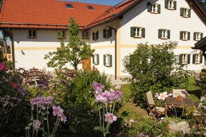 A building with a red-tiled roof and multiple windows with green shutters. There is a garden with various flowers and a table and chairs set outside. - Romantik Hotel Chalet am Kiental (Herrsching am Ammersee)