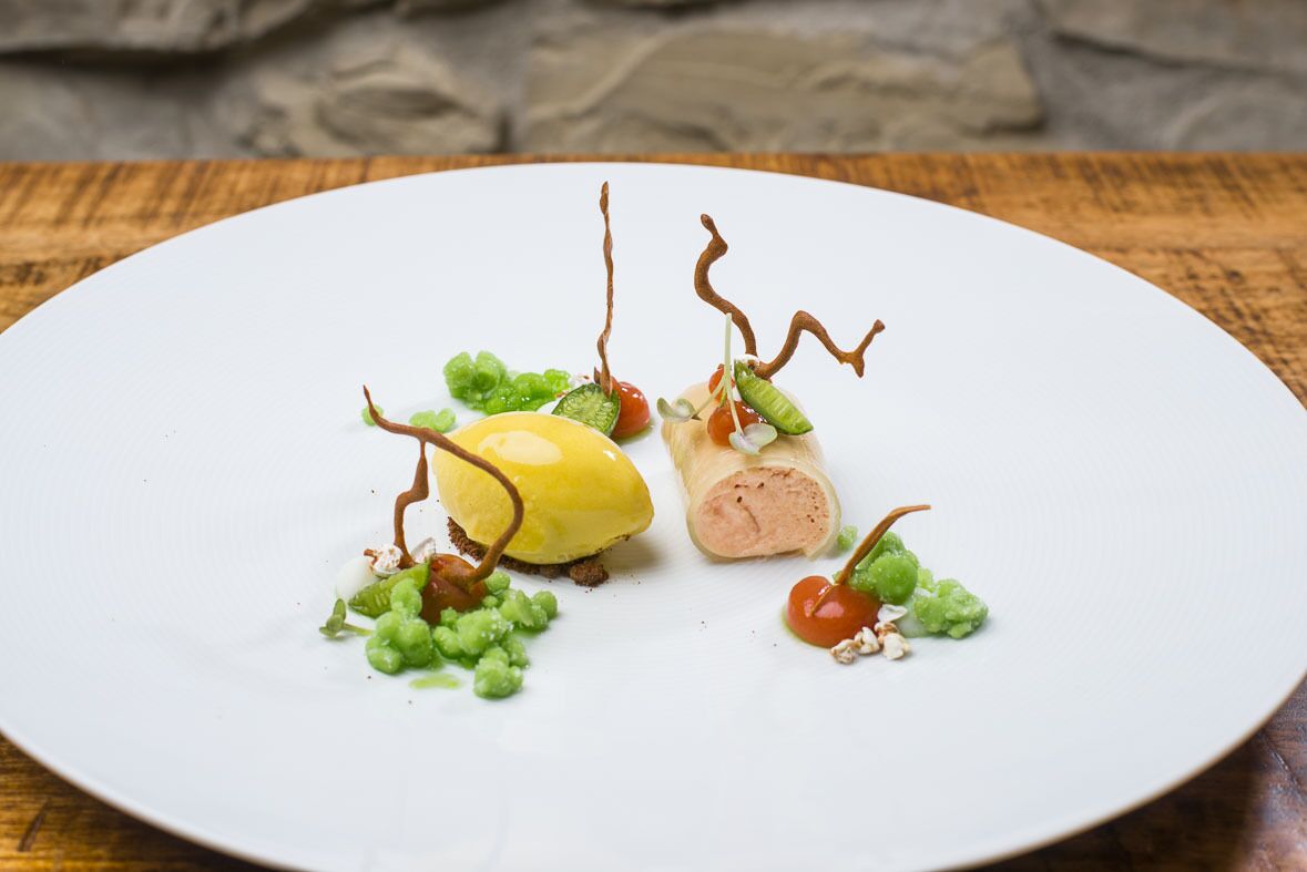 Ein weißer Teller mit einem Dessert aus gelber Kugel, gerolltem Gebäck und grünen Garnituren.