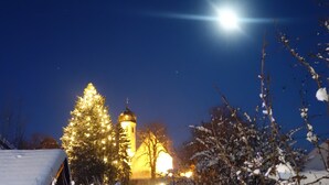 A snow-covered landscape with a church illuminated by lights, a snow-covered tree, and a stone wall. - Romantik Hotel Chalet am Kiental (Herrsching am Ammersee)