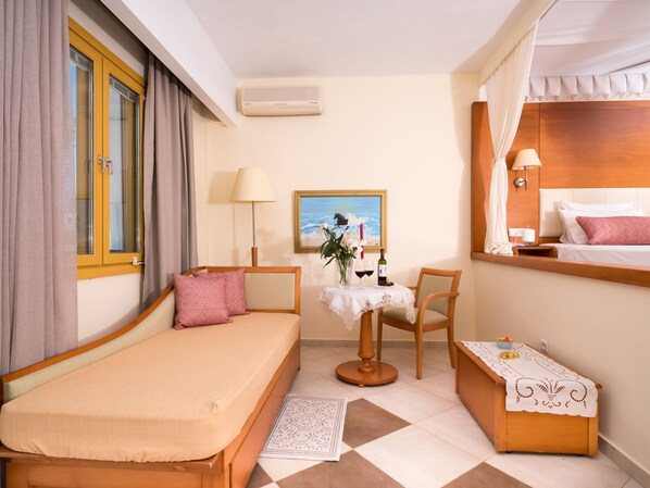 A hotel room with a bed, a desk with a chair, a small table with a vase of flowers, and a painting on the wall.